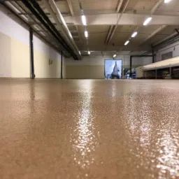 Beżowa, błyszcząca posadzka w hali przemysłowej w Olkuszu, widoczne rury pod sufitem i brama w tle.