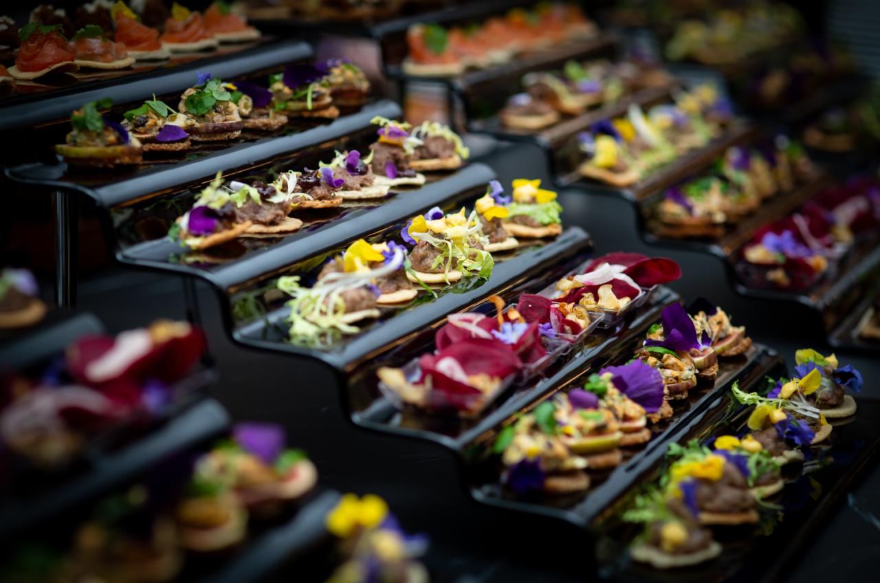 Elegancko podane, różnorodne przekąski na czarnych, schodkowych półmiskach, udekorowane jadalnymi kwiatami i ziołami.
