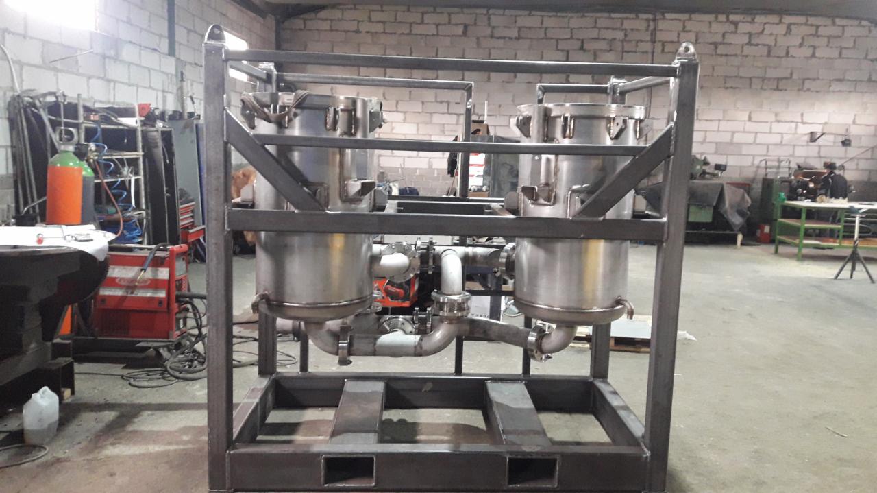 Konstrukcja stalowa z czterema zbiornikami ze stali nierdzewnej i rurami, widoczna w warsztacie z ceglanymi ścianami i sprzętem spawalniczym w tle.