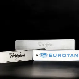 Metalowe tabliczki z logo firm Whirlpool i Eurotanks, wykonane z r&oacute;żnych materiał&oacute;w i technik, leżące na czarnym tle.