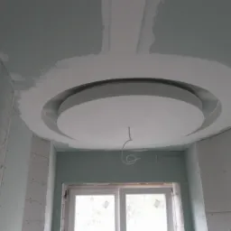 Niedokończony sufit z płyt kartonowo-gipsowych z okrągłą dekoracją i wystającym przewodem elektrycznym, widoczne łączenia płyt wymagające szpachlowania.