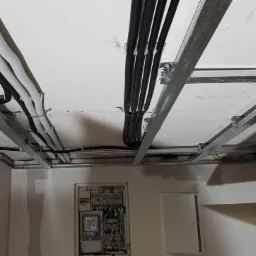 Montaż metalowej konstrukcji sufitu podwieszanego z widocznymi kablami i rurami instalacyjnymi w nowym budynku.