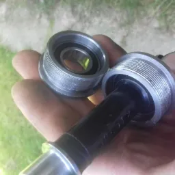 Dwa metalowe pierścienie z gwintem wewnętrznym oraz czarny element łączący, trzymane w dłoni na tle trawy.