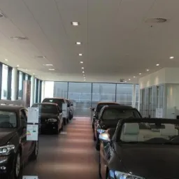 Wnętrze salonu samochodowego z rzędem zaparkowanych, nowych samochodów marki BMW, oświetlone systemem paneli LED w suficie podwieszanym.