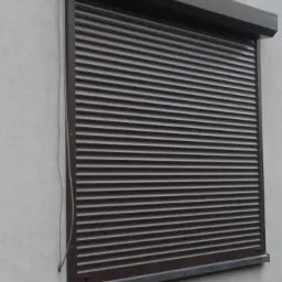 Zamknięta, brązowa roleta zewnętrzna na szarej ścianie budynku, widoczne prowadnice i kaseta rolety.