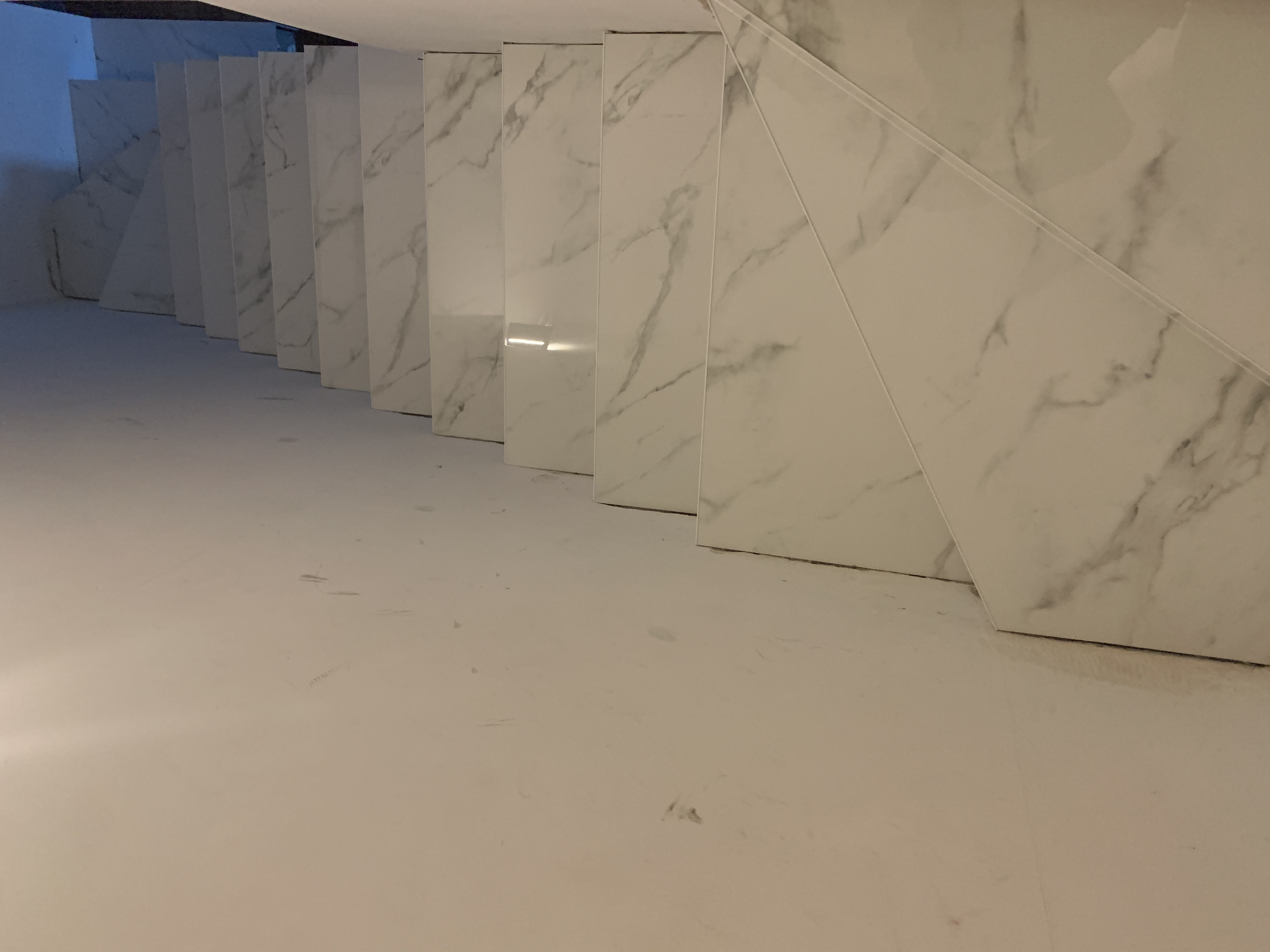 Wykończona łazienka ze ścianami i podłogą wyłożonymi białymi płytkami imitującymi marmur, widok z dołu na wnękę.