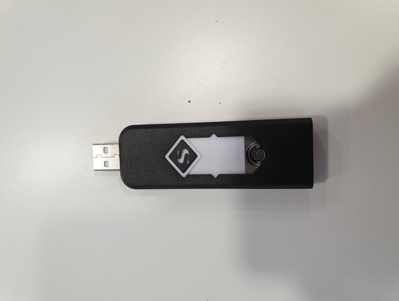 Czarny pendrive USB z logo firmy w kształcie rombu z literą 'S' i spiralnym wzorem obok, leżący na białym tle.