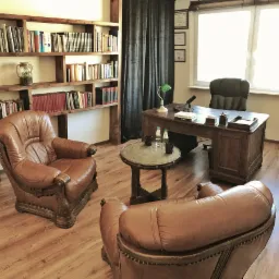 Gabinet z dębowym biurkiem, skórzanymi fotelami, regałem z książkami i zieloną lampką na biurku, sugerujący atmosferę do rozmów i refleksji.