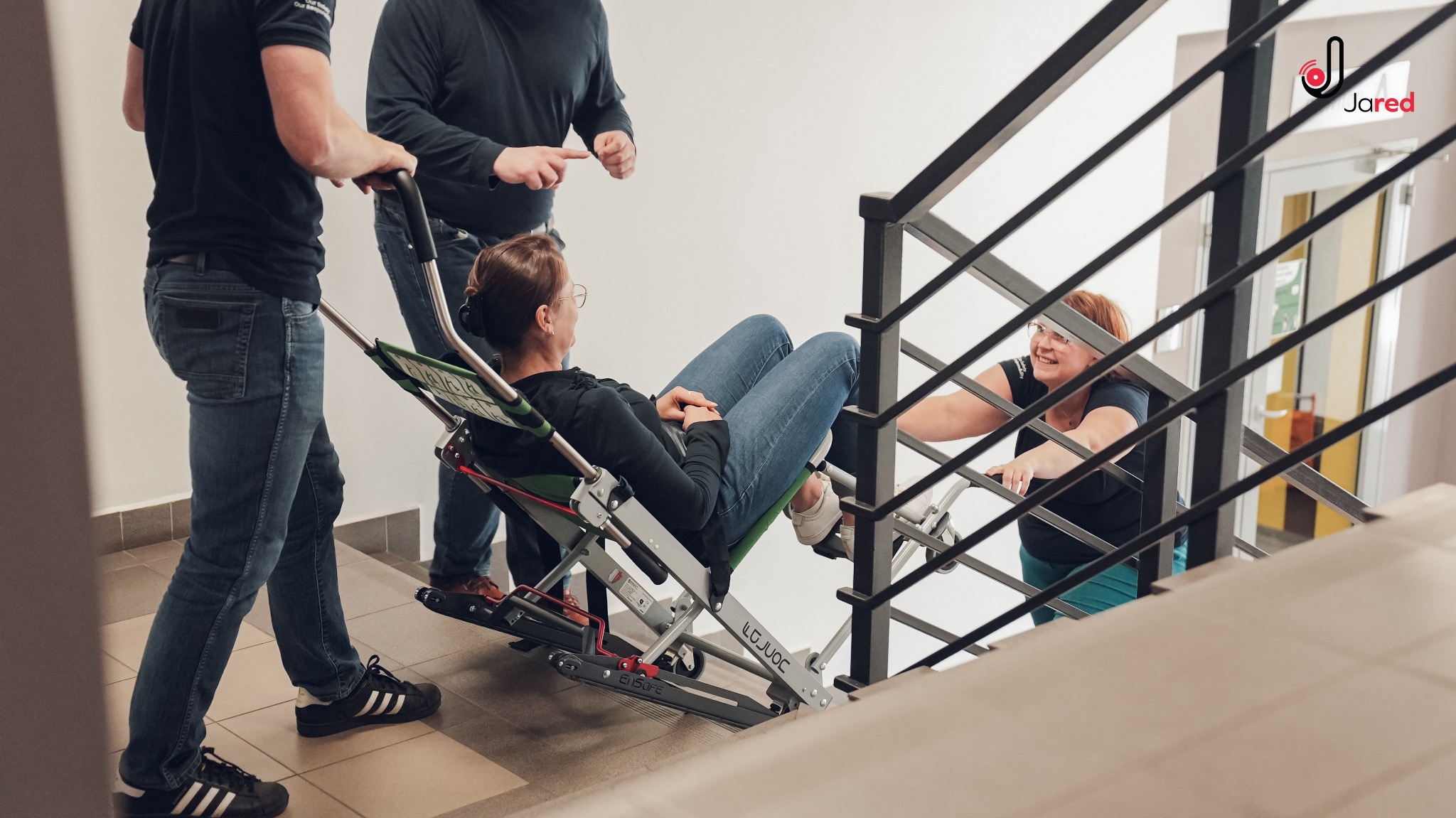 Instruktorzy demonstrują transport osoby niepełnosprawnej po schodach przy użyciu krzesła ewakuacyjnego podczas kursu pierwszej pomocy.