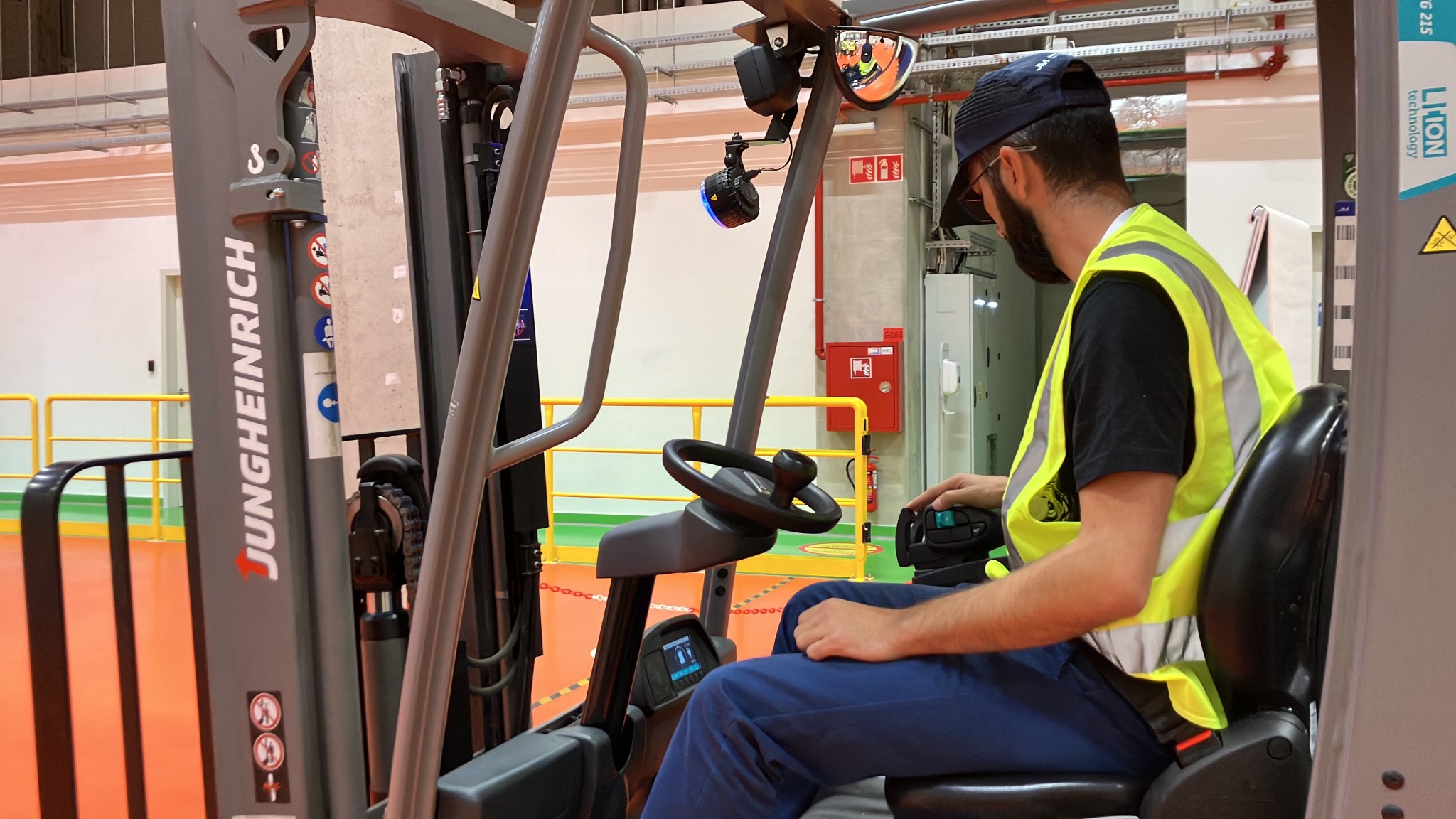 Operator w kamizelce odblaskowej siedzi w wózku widłowym marki Jungheinrich, przygotowując się do transportu towarów w magazynie.