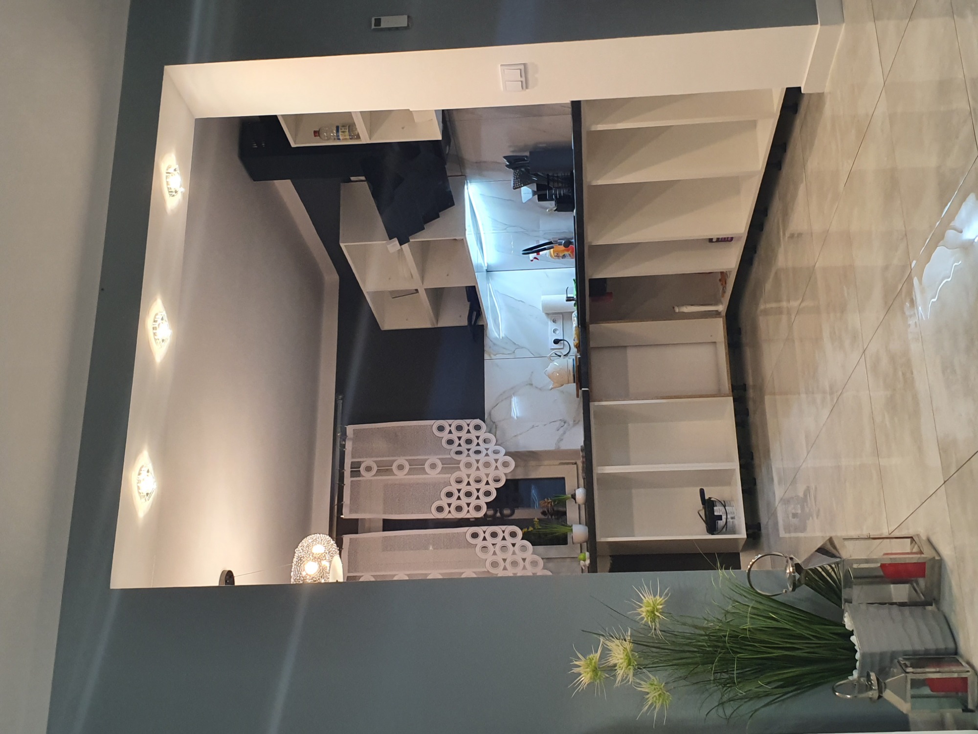 Wykończone wnętrze garderoby z białymi półkami, marmurowymi płytkami i dekoracyjnym oświetleniem punktowym