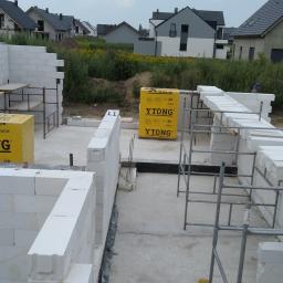 Korta - Budowa domu jednorodzinnego w trakcie wznoszenia ścian fundamentowych z bloczków Ytong; widoczne rusztowania i zapas materiału.