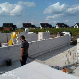 Korta - Budowa ścian fundamentowych z bloczków betonu komórkowego Ytong na tle domów jednorodzinnych, widoczni pracownicy budowlani.