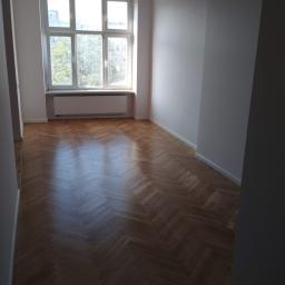 Korta - Pusty pokój po odnowieniu z nową drewnianą podłogą w jodełkę, świeżo pomalowanymi ścianami na biało i dużym oknem z widokiem na drzewa.