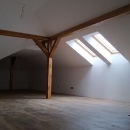Korta - Poddasze po remoncie, z drewnianą konstrukcją nośną, trzema oknami dachowymi wpuszczającymi jasne światło, świeżo położonymi panelami podłogowymi i gładkimi, białymi ścianami.