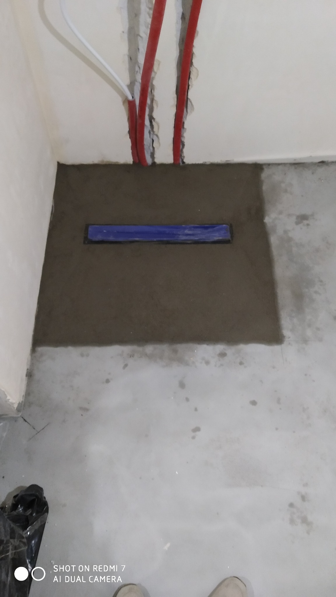 Ukończona instalacja odpływu liniowego w posadzce łazienki, z widocznymi rurami instalacji wodnej w ścianie.