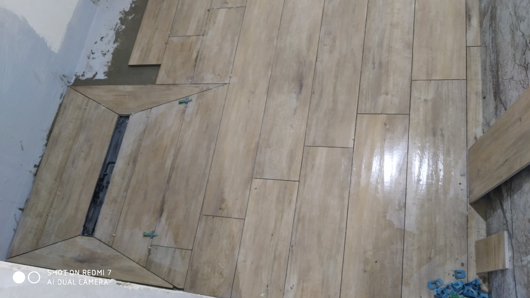 Układanie podłogi z płytek imitujących drewno, z widocznym odpływem liniowym w rogu pomieszczenia. Użyto klipsów poziomujących.