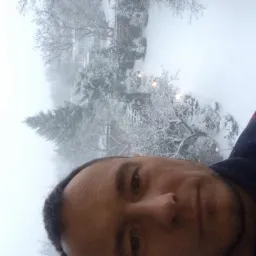 Autoportret mężczyzny w swetrze z wzorem na tle zasypanego śniegiem ogrodu i drzew we mgle.