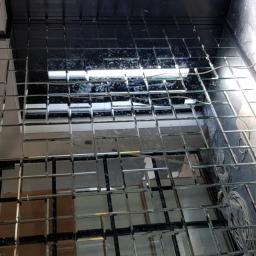 Zbiglass - Montaż mozaiki lustrzanej z kwadratowych płytek na ścianie, widoczne kable i narzędzia montażowe, w trakcie prac wykończeniowych.