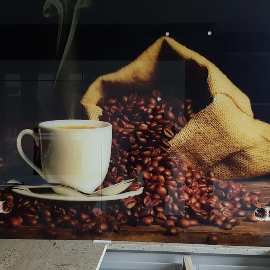 Szklana ściana nad blatem kuchennym z grafiką przedstawiającą filiżankę kawy i wysypujące się ziarna kawy z jutowego worka.