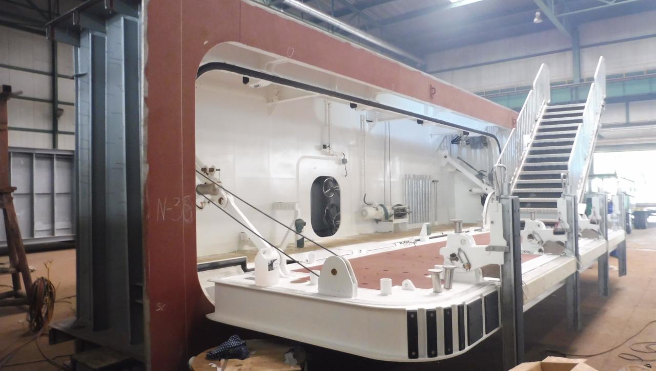 Wnętrze dużej, białej konstrukcji z metalu z elementami w kolorze czerwonym, widoczne schody i metalowe podpory, oświetlenie przemysłowe w tle.