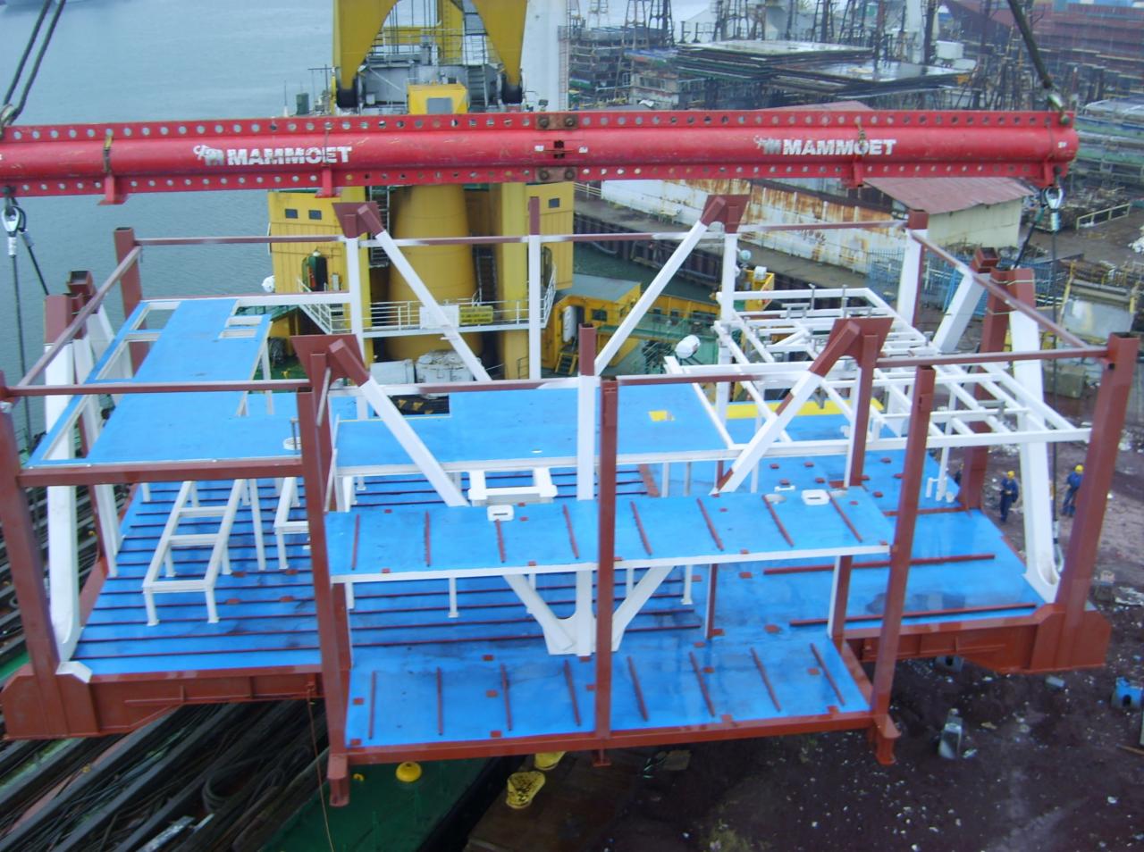 Platforma stalowa z niebieskim wypełnieniem podnoszona przez dźwig z logotypem firmy Mammut, widok z góry na konstrukcję w trakcie transportu.