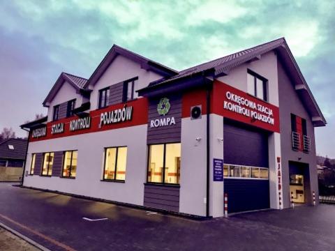 Budynek okręgowej stacji kontroli pojazdów z nazwą 'ROMPA' i logo recyklingu na elewacji, widok z zewnątrz po zmroku.