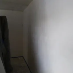 Wnętrze pokoju po nałożeniu gładzi, z widoczną folią ochronną na podłodze i taśmą malarską wzdłuż krawędzi podłogi.