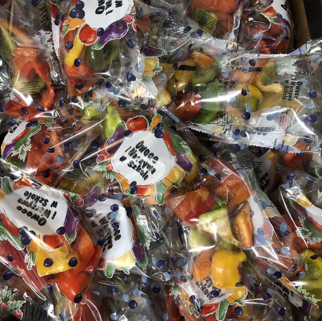 Pojedyncze porcje pokrojonych papryk w przezroczystych, zamkniętych woreczkach z nadrukiem 'Owoce i Warzywa w Szkole', ułożone w większym pojemniku.