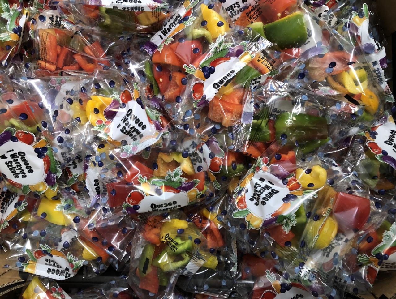 Pojedynczo zapakowane porcje pokrojonej papryki w przezroczystych foliowych woreczkach z etykietą 'Owoce i Warzywa w Szkole', ułożone w kartonie.