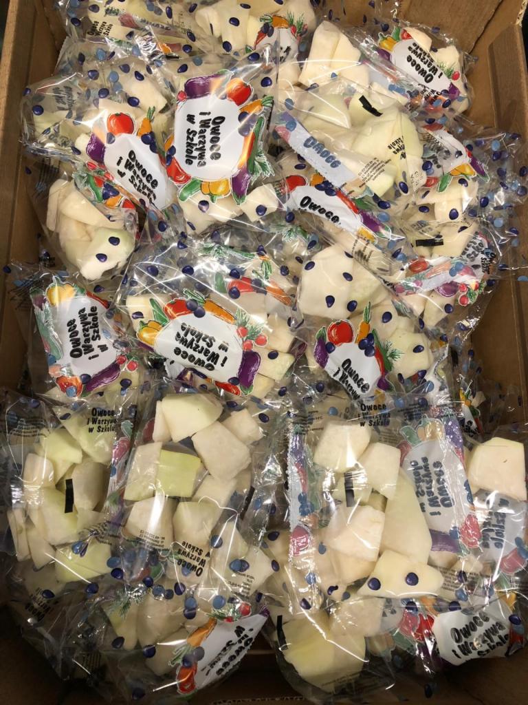 Karton wypełniony pojedynczo zapakowanymi porcjami pokrojonych jabłek w przezroczystych foliowych woreczkach z nadrukiem 'Owoce i Warzywa w Szkole'.