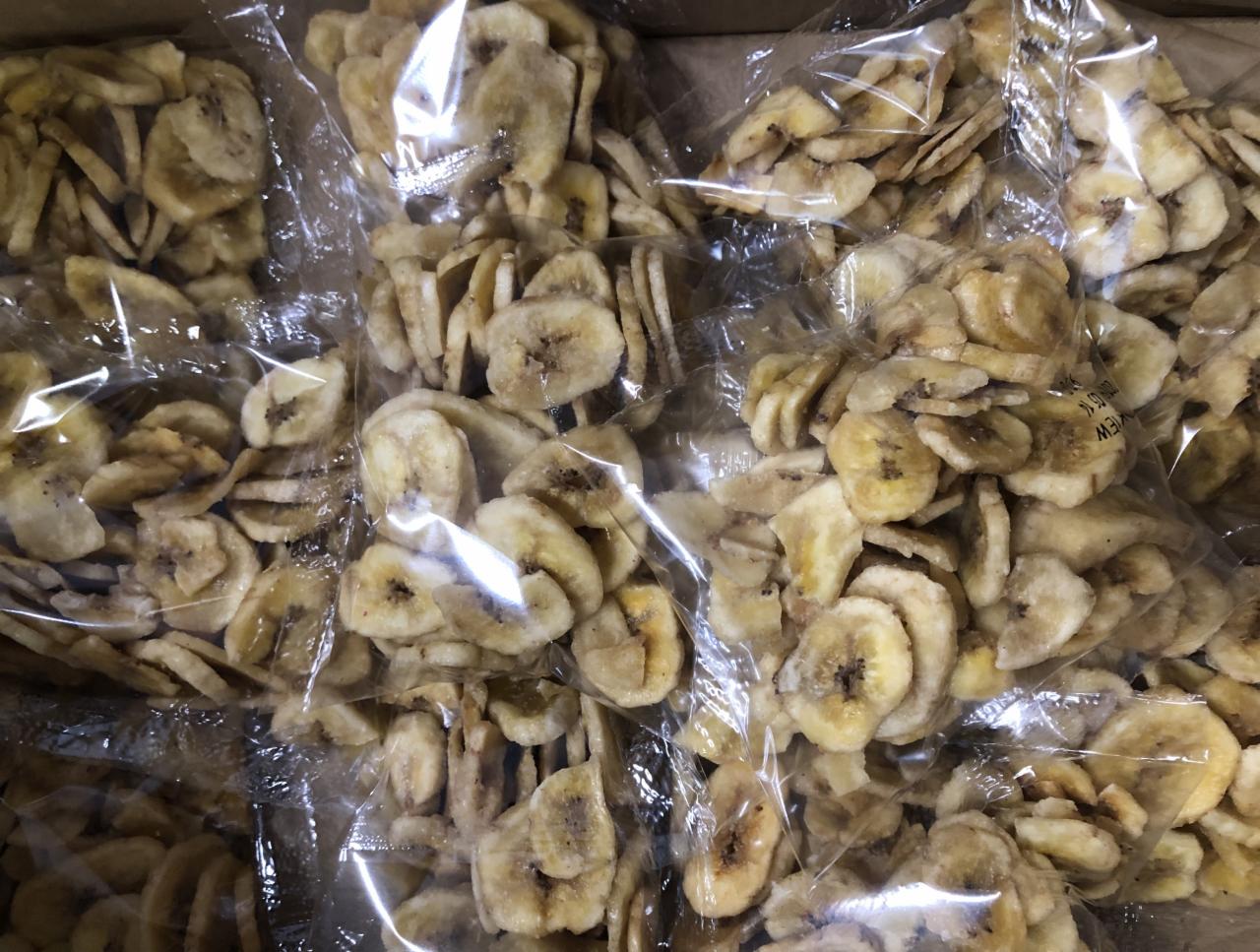 Karton wypełniony przezroczystymi torebkami z suszonymi plasterkami bananów, widoczne detale tekstury owoców i zgrzew torebki.