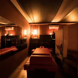 Pokój zabiegowy z czerwonym łóżkiem do masażu, lustrami na ścianie, dekoracyjną figurką Buddy i subtelnym oświetleniem.