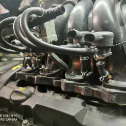 Widok z bliska na kolektor ssący silnika spalinowego z podłączonymi wtryskiwaczami i przewodami, prawdopodobnie podczas montażu lub serwisu.