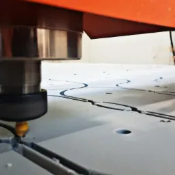 Frezarka CNC w Gdańsku wycina okrągłe elementy z szarego tworzywa, widoczne wióry i logo firmy Starmax Ploter CNC w prawym górnym rogu.