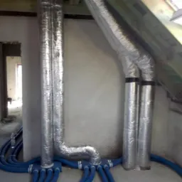 Montaż instalacji rekuperacji w surowym stanie poddasza w Goszczynie, widoczne rury aluminiowe i niebieskie przewody wentylacyjne.