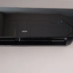 Czarny klimatyzator AUX zamontowany na białej ścianie z dekoracyjnymi listwami, widoczny wyświetlacz i logo producenta.