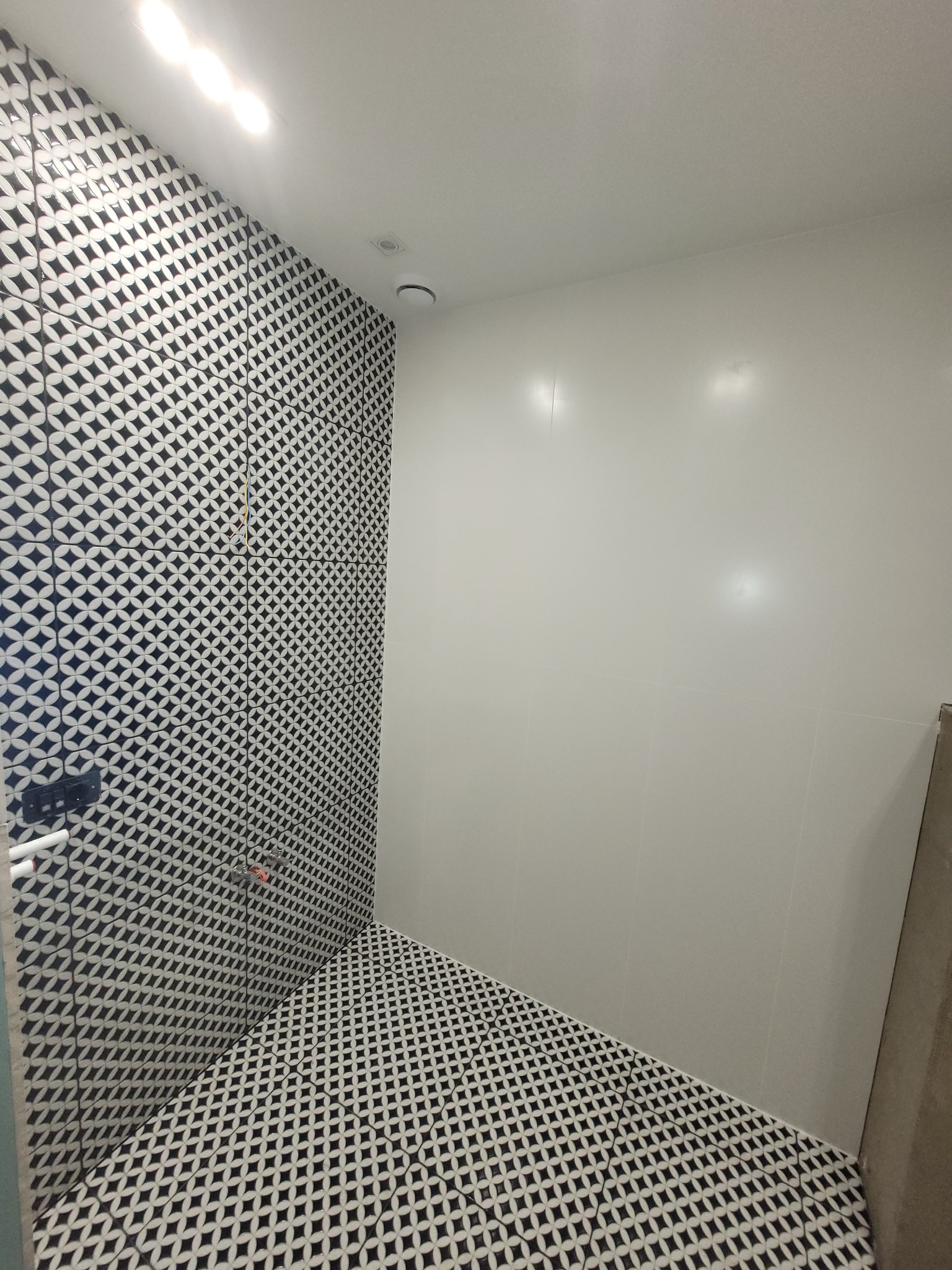 Wykończona łazienka z geometrycznymi czarno-białymi płytkami na ścianie i podłodze, kontrastująca z gładką, jasną ścianą bez płytek.