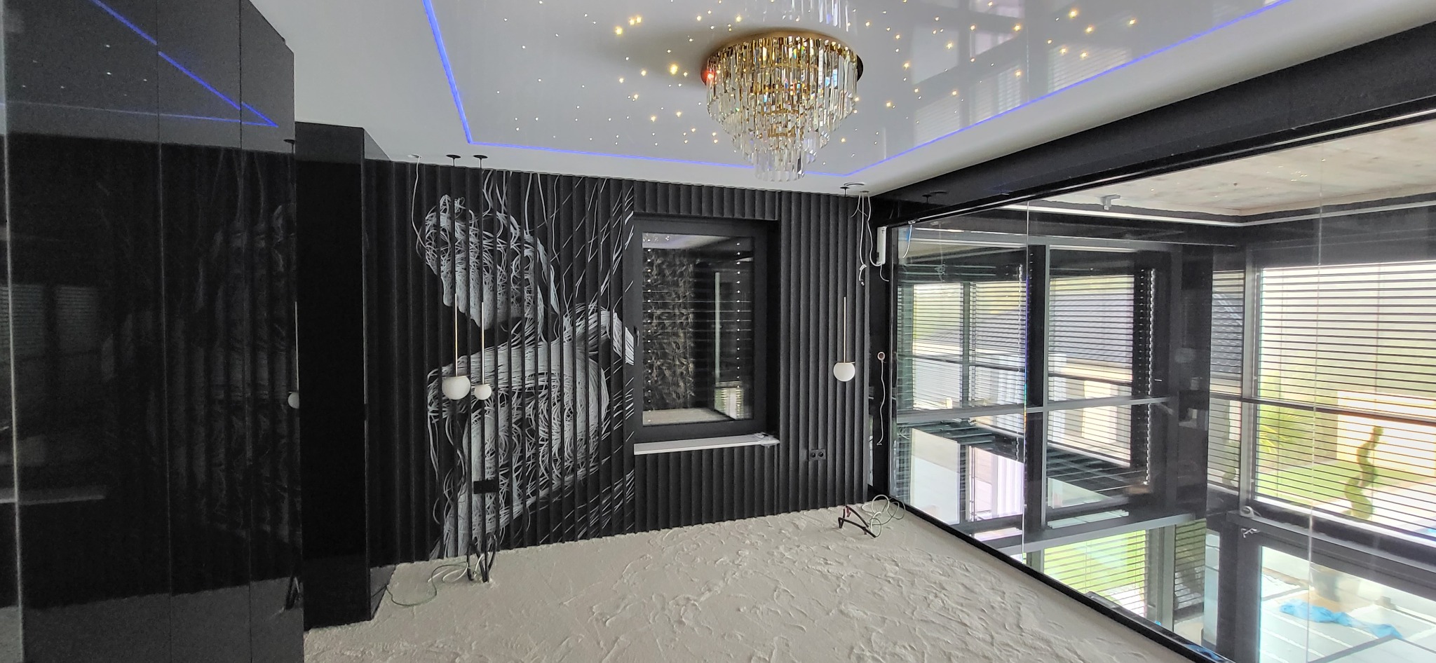 Nowoczesne wnętrze z czarną ścianą z grafiką, podwieszanym sufitem z oświetleniem LED i kryształowym żyrandolem, w trakcie wykańczania podłogi.