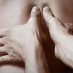 Dłonie terapeuty uciskające dolną część pleców pacjenta, widoczne z bliska, w tle zarys sylwetki.