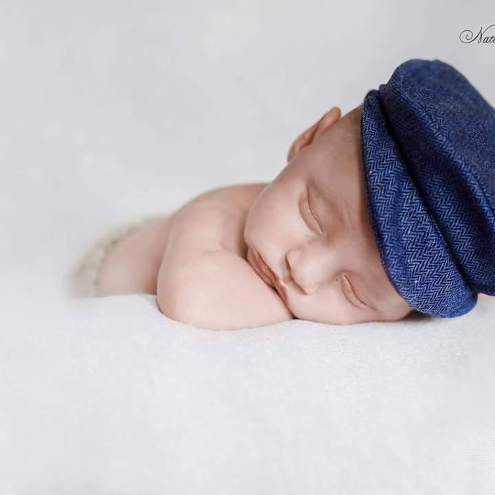 Śpiący noworodek w niebieskiej czapce z jodełkowym wzorem na białym tle.