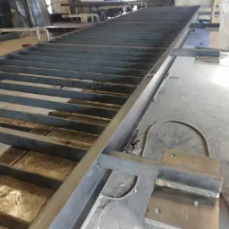 Metalowa konstrukcja schodów w trakcie budowy w warsztacie, widoczne spawy i elementy mocujące.