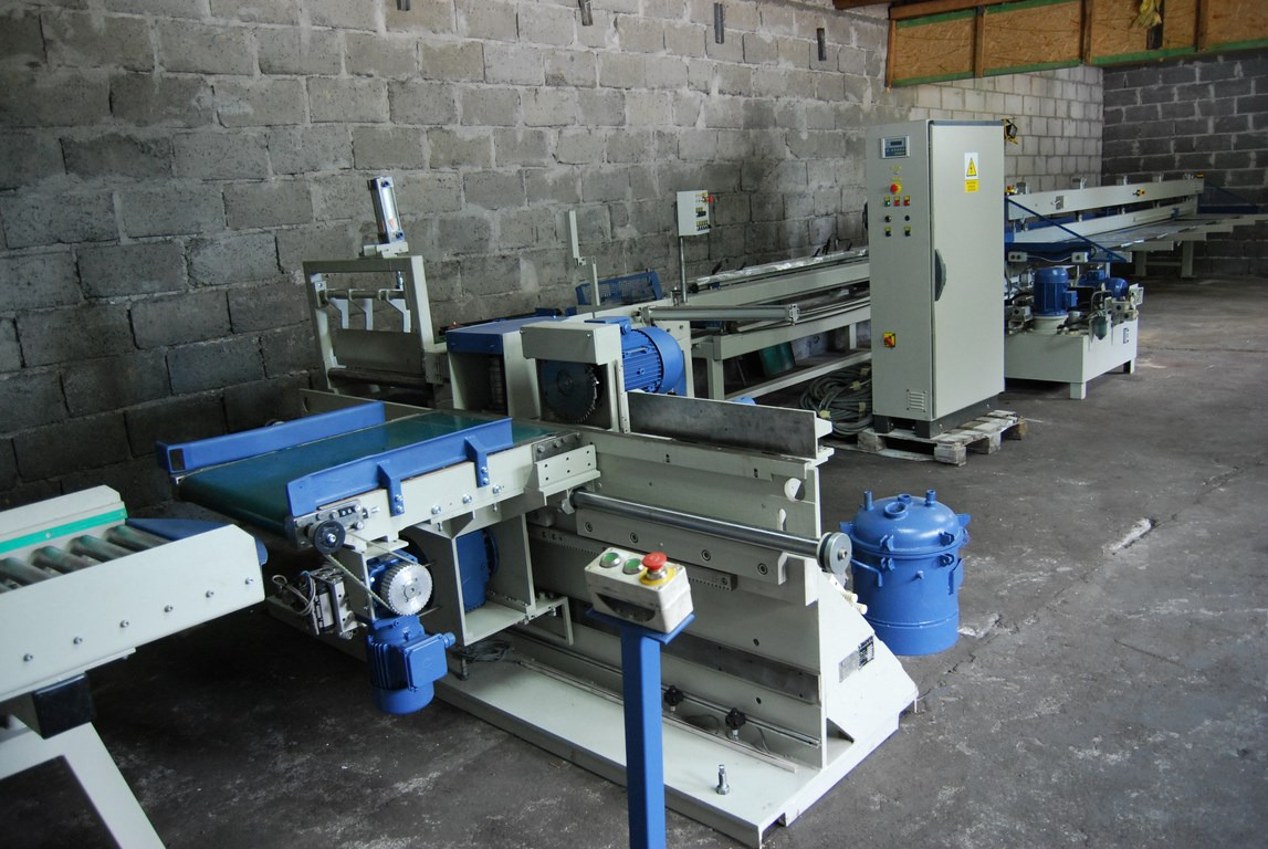 Linia do łączenia drewna FAMAD PDFD-I z widocznym panelem sterowania i niebieskim zbiornikiem, ustawiona w hali o surowych, betonowych ścianach.