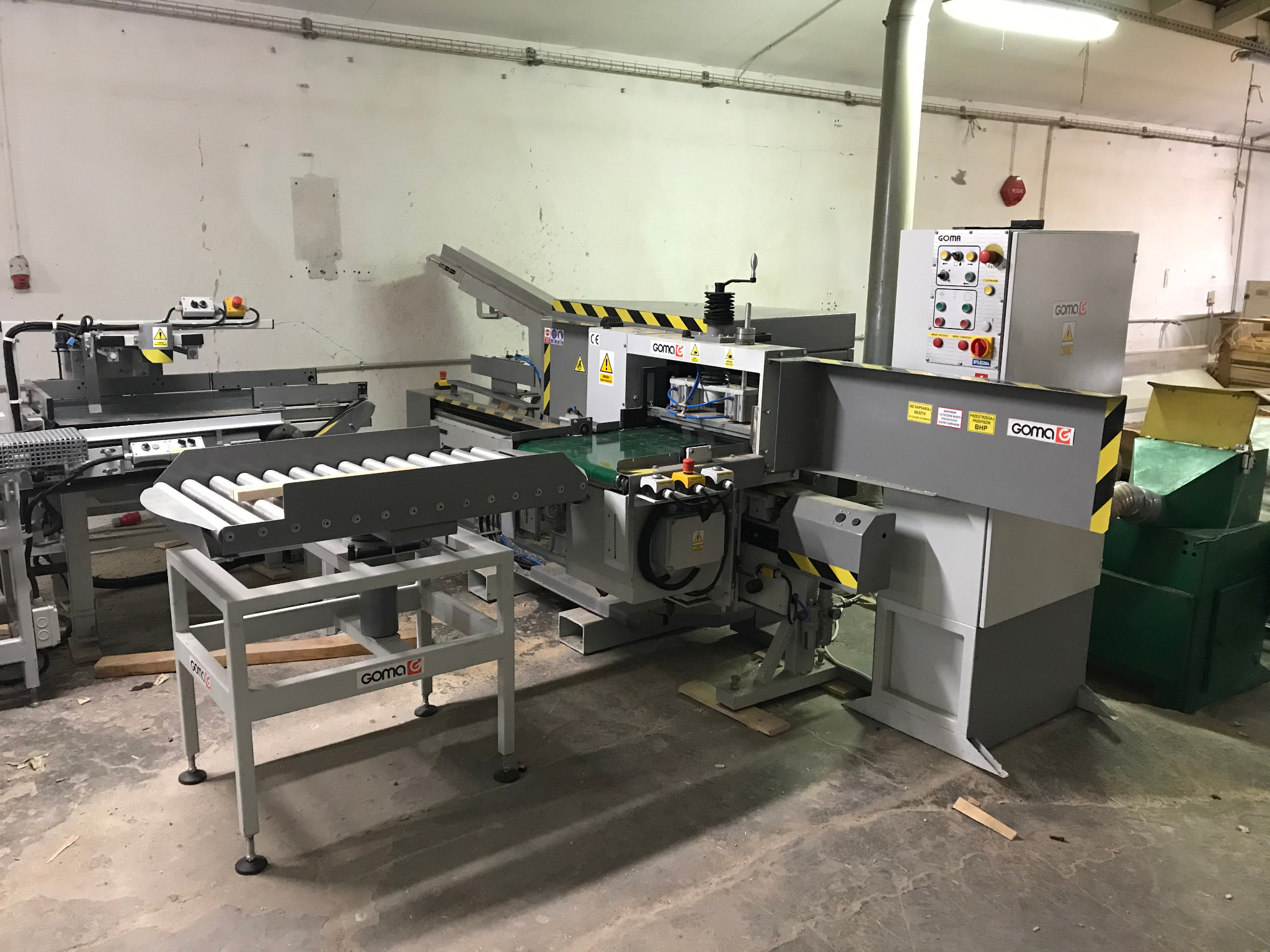 Linia do łączenia drewna Goma FC-10 KZ6 + FC-10 PZ6/2, widok z boku, z widocznymi elementami sterującymi i podajnikami rolkowymi, ustawiona w hali produkcyjnej z surowymi ścianami.