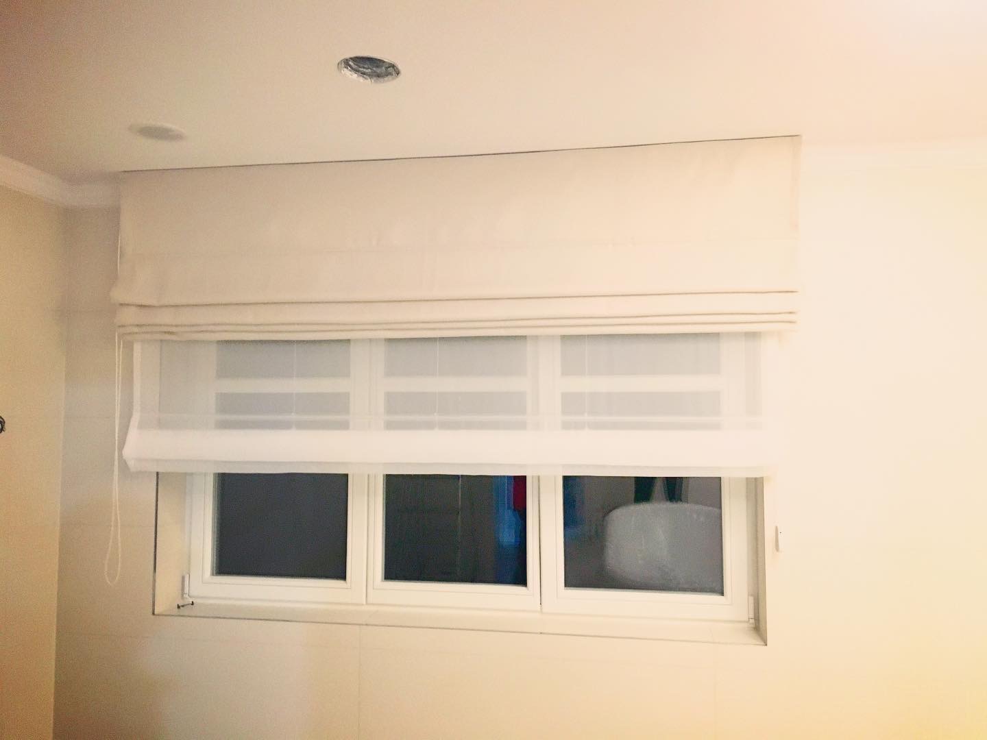 Beżowa, rzymska roleta z delikatnymi marszczeniami, zamontowana w białym oknie w jasnym pomieszczeniu.