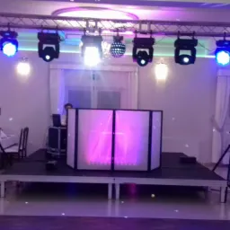 Scena z nagłośnieniem i oświetleniem w sali bankietowej, reflektory LED na kratownicy, kolumny głośnikowe na statywach po bokach, DJ za podświetlanym panelem, parkiet.