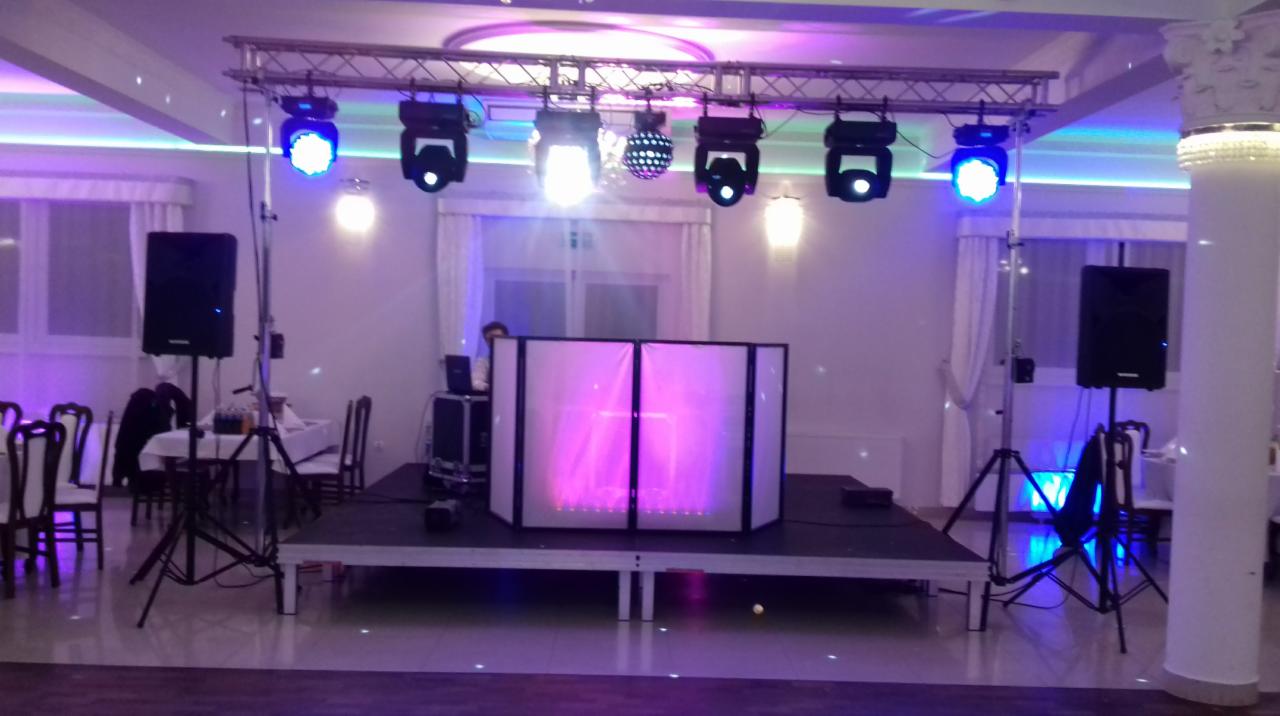 Scena z nagłośnieniem i oświetleniem w sali bankietowej, reflektory LED na kratownicy, kolumny głośnikowe na statywach po bokach, DJ za podświetlanym panelem, parkiet.