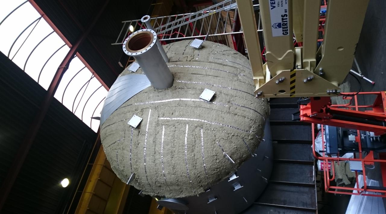 Izolacja termiczna zbiornika przemysłowego w Chojnie, widok z góry na ocieploną powierzchnię z widocznymi elementami mocującymi izolację i fragmentem podnośnika koszowego.