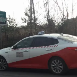 Biało-czerwona taksówka Okay Taxi zaparkowana przy znaku drogowym Kęty, widoczny numer telefonu.
