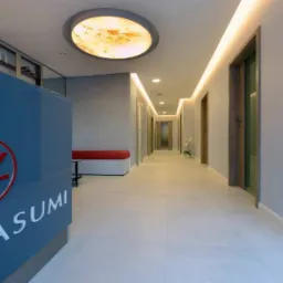 Recepcja w nowoczesnym biurze z logo Yasumi, podświetlany sufit z motywem marmuru, długi korytarz z szeregiem drzwi i oświetleniem LED.